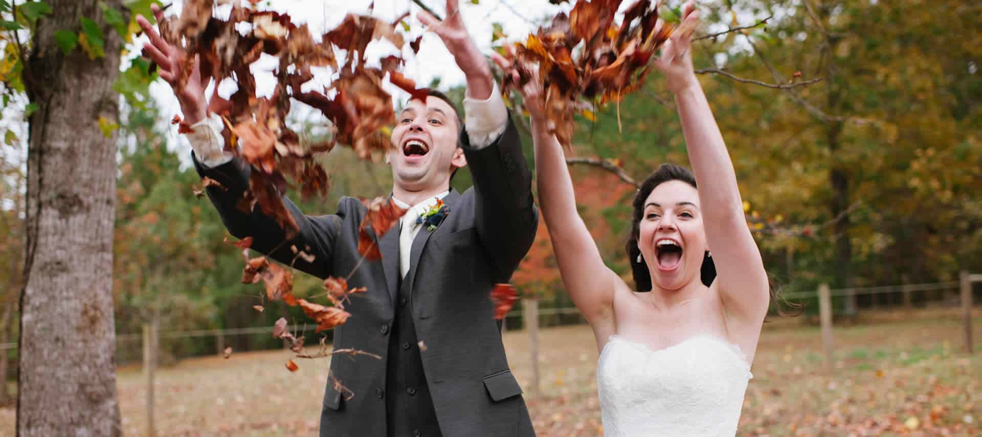 Young and happy bride and groom throw autumn leaves up into the air exuberantly.