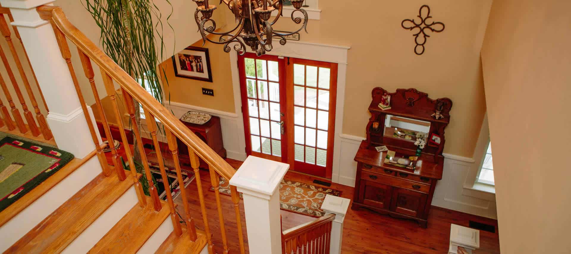 View of foyer from staircase landing - wooden floors, wooden star rails and an antique dresser.
