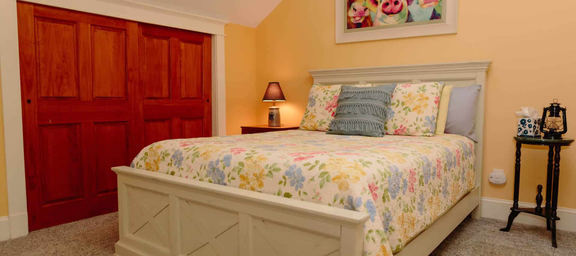 Farmhouse white sleigh bed with a flowered spread and severall pillows in a yellow bedroom.
