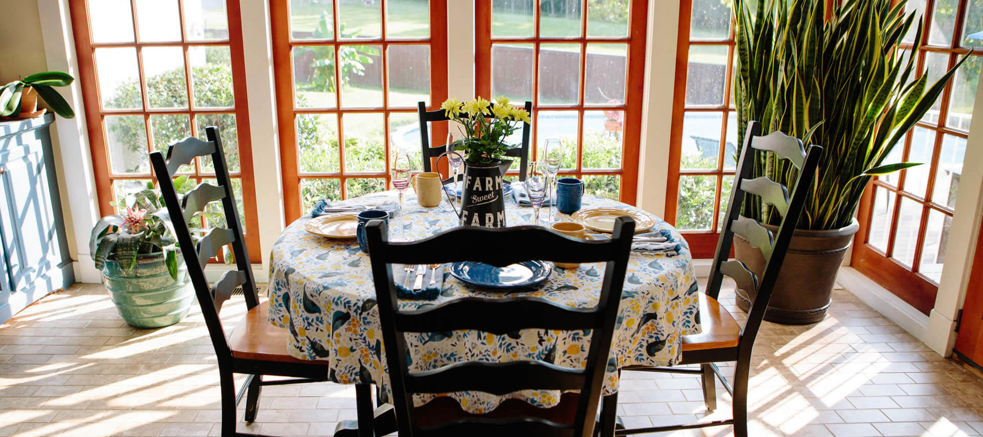 Small four-top table with a flowered cloth in front of a large window in a bright and airy breakfast room