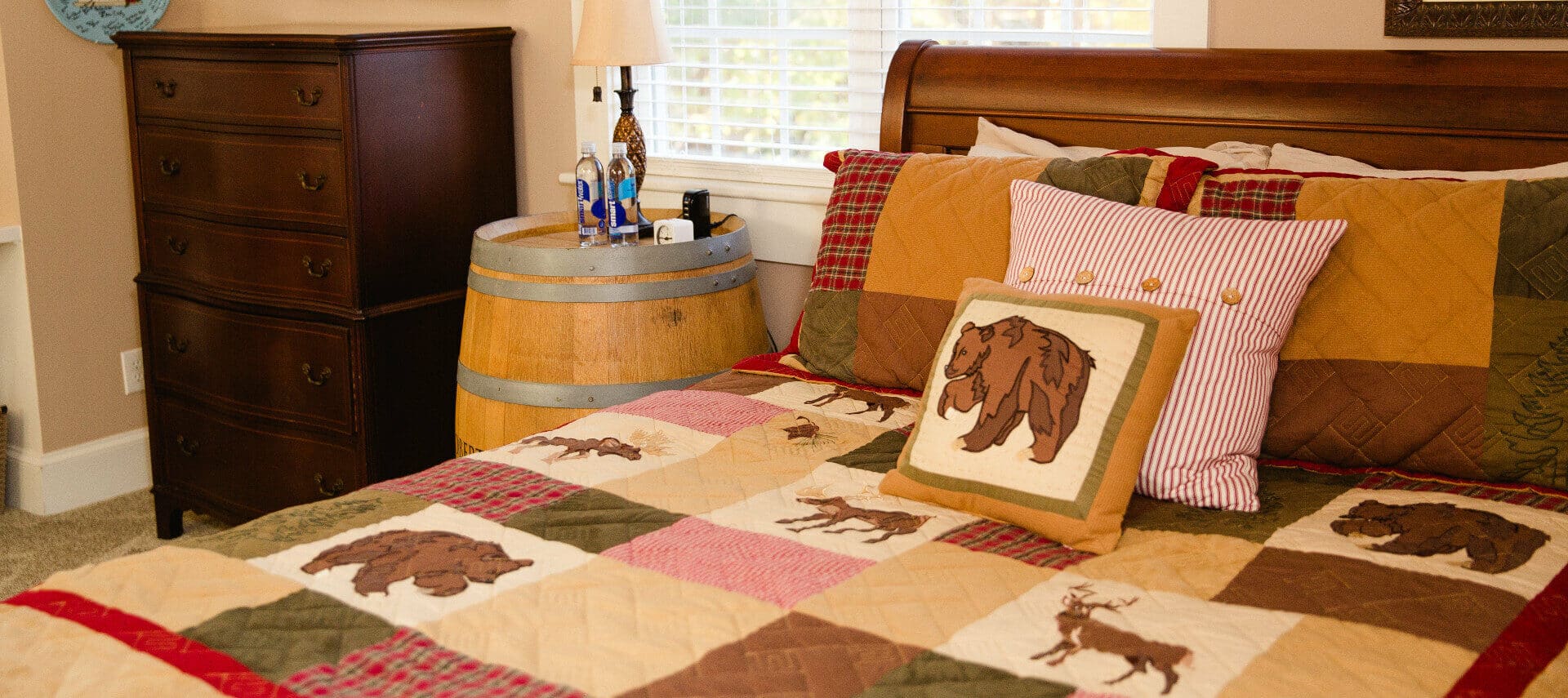 Cherry sleigh bed by window with a forest animals quilt in tan and red with a Robert Mondavi wine barrel as a nightstand, high cherry dresser in corner.
